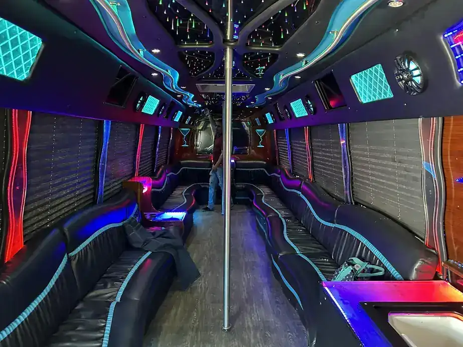 Party bus interior lit pink and teal, black leather lounge seating down both sides